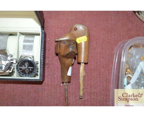 A walking stick top in the form of a dog together with one other in the form of a duck with glass eyes