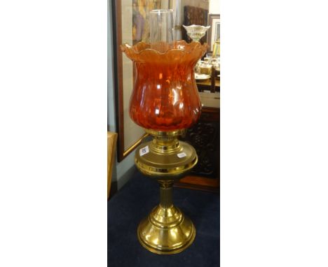 An oil lamp, with brass base, red shade and funnel, maximum height 52cm.