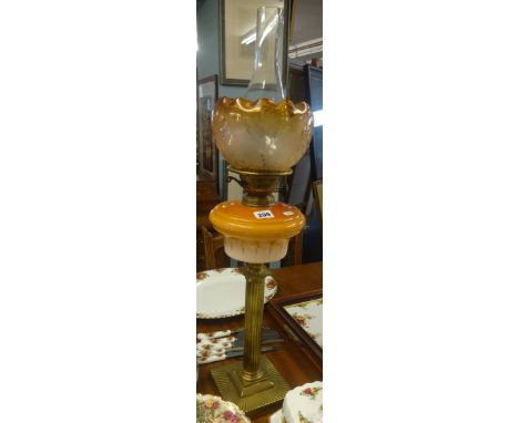 An oil lamp with Corinthian column base, glass reservoir and orange shade with funnel, maximum height 74cm.