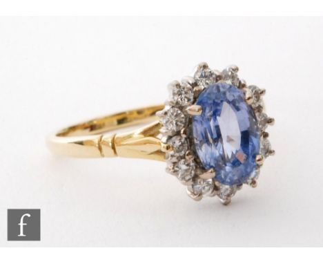 An 18ct hallmarked sapphire and diamond cluster ring, central oval cornflower blue sapphire, length 10mm, within a twelve sto