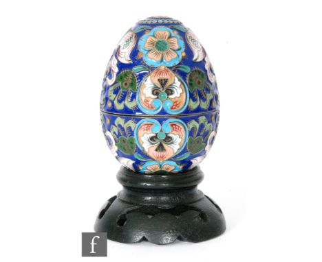 A Russian silver and enamelled cloisonne Easter egg decorated with tonal green and pink foliate scrolls to a navy blue ground