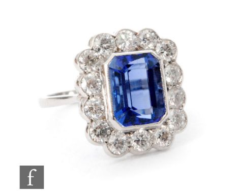 A 18ct white gold tanzanite and diamond cluster ring, central emerald cut tanzanite, length 9.5mm, within a border of fourtee