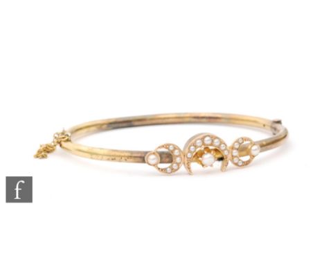An early 20th Century 9ct hinged bangle set with seed pearl crescents to the centre, weight 8g. 