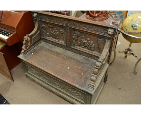 An oak carved monks bench with carved panels and a lift up seat