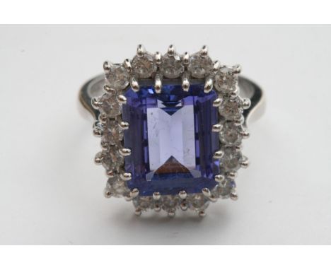 An 18ct white gold ring set with a large Tanzanite, Emrald cut, Central stone surrounded by a row of diamonds.