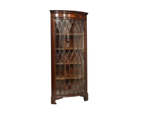 20th Century mahogany floor standing bowfront corner cabinet, the moulded dentil cornice over glazed tracery door enclosing t