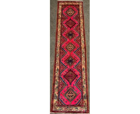 A North west Persian Heriz runner carpet, hand-knotted with a central row of seven diamond form medallions, in vibrant colour