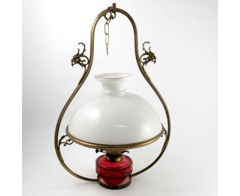 A brass hanging oil lamp, with white glass shade and ruby glass oil reserve, the brass frame with scroll decoration, height 2