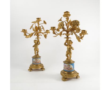 A pair of continental ormulu and Sevres style three light candelabra, decorated with foliage supported by putti with a porcel