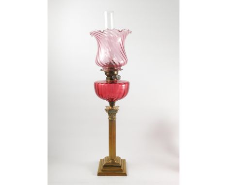 A ruby glass and brass table lamp, the brass Corinthian column with ruby glass oil reserve and wrythern moulded cranberry gla