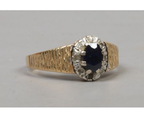 A retro 18ct gold ring with textured shoulders and set with a sapphire under a border of diamonds, size N.