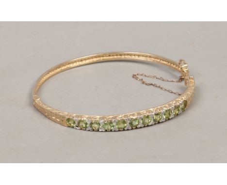 A yellow metal bangle with scroll work shoulders set with peridot and diamonds, 12.82 grams (AF).