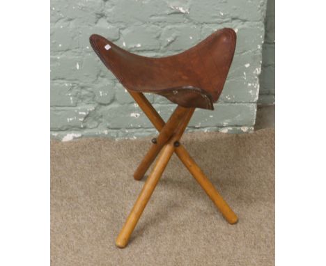 A folding tripod stool with leather seat.