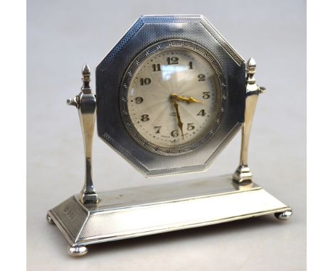 An engine-turned silver desk clock, the textured silvered dial in octagonal frame, swivelling on pillar and platform stand wi