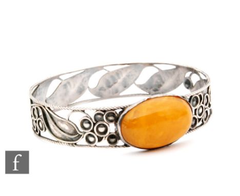 A mid 20th Century pierced white metal and amber slave bangle, oval cabachon central amber to a leaf border, diameter 9cm, we