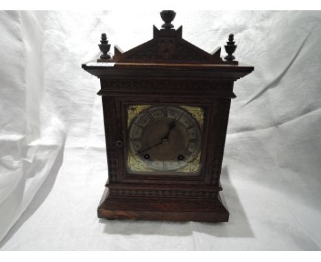 A late Victorian/Edwardian oak cased mantel clock having carved and spindle decoration with spandrel design face and striking