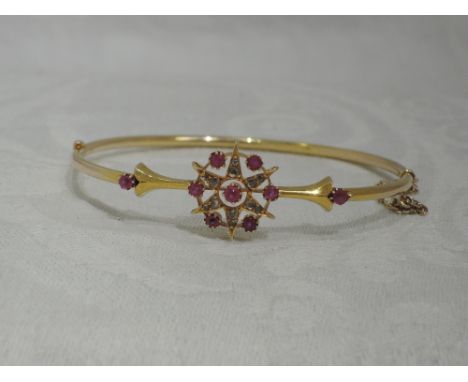 A Victorian yellow metal hinged tubular bangle stamped 15ct having ruby and diamond star burst decoration with ruby set mould