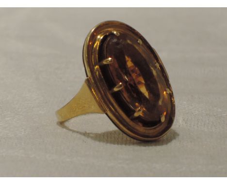 A lady's dress ring having an oval citrine style stone in a claw set collared mount on a  yellow metal loop stamped 18K,  siz