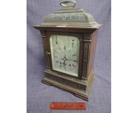 A late Victorian/Edwardian stained case mantel clock having carved foliate decoration and cane handle over silver Roman numer