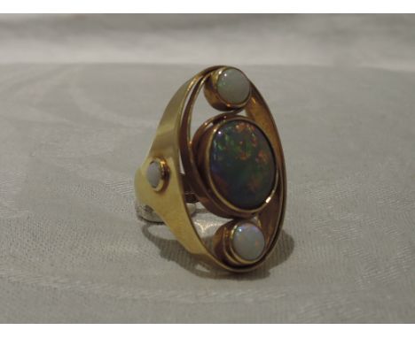 A lady's dress ring of stylised form having a large central opal in a collared swirl setting flanked by two further opals in 