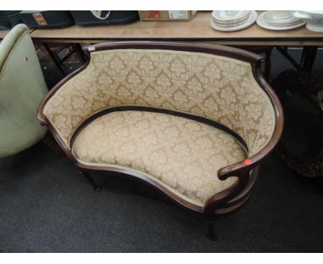 An Edwardian mahogany salon settee of sweep design having later beige upholstery on tapered legs