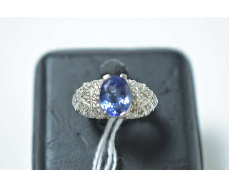 A contemporary white metal, tanzanite and diamond cocktail ring, having a central oval cut tanzanite, pellet-set above Gothic