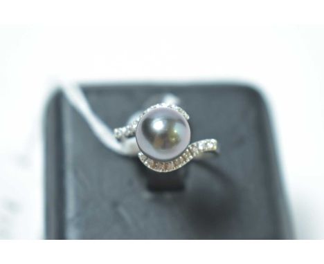A contemporary black pearl and diamond cocktail ring, having a central pearl sphere, set within bifurcated and channel set di