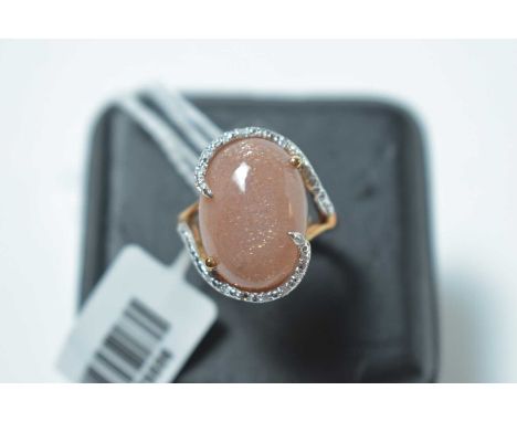 A goldstone and diamond ring, the oval goldstone cabochon within diamond scroll mount, on 9ct yellow metal shank. 