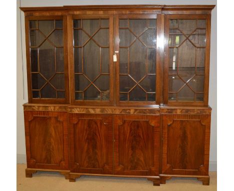 A 20th Century mahogany breakfront bookcase, the projecting dental-moulded cornice above four astragal-glazed doors enclosing