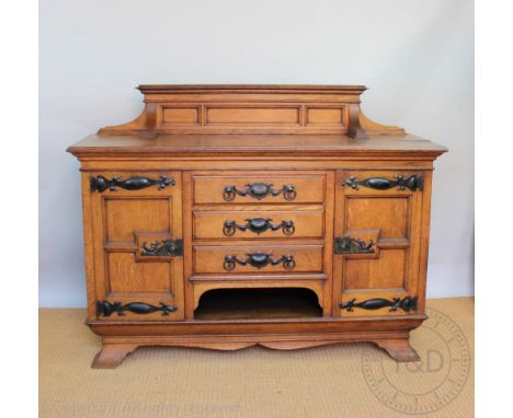 An Arts and Crafts oak sideboard, in the manner of Liberty and Co, with raised back above three drawers and two cupboard door