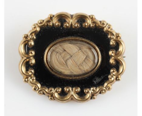 A Victorian enamel memorial brooch, featuring a glass fronted panel containing plaited hair, surrounded by black enamel and a