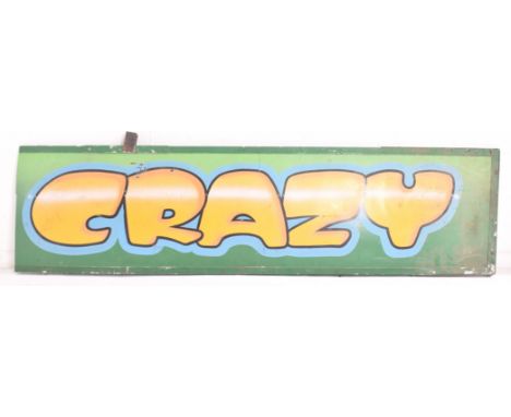 A vintage funfair / amusement park / fairground oversized wooden board sign reading CRAZY. The sign on green ground with yell