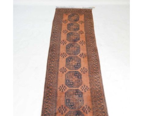 An Eastern woollen runner, with a row of central medallions, on a red ground301w x 80d cm
