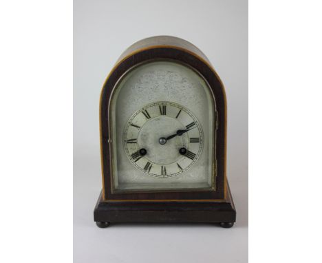 An early 20th century oak veneered domed mantel clock, the silverised dial with Roman numerals and floral scroll engraved spa