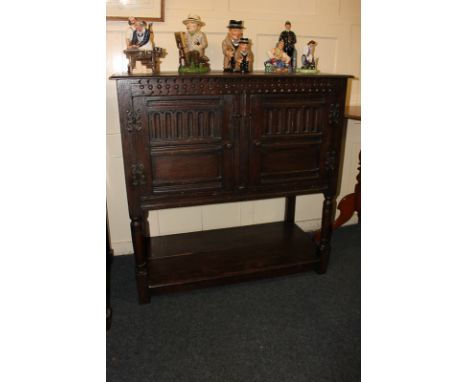 A 20th century carved oak cabinet with rectangular top above two panelled doors, on turned supports with low shelf on block f