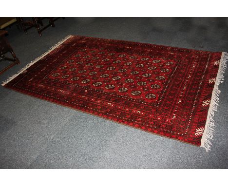 A Bokhara wool carpet with five rows of nine elephant feet motifs, surrounded by geometric and floral borders in shades of re