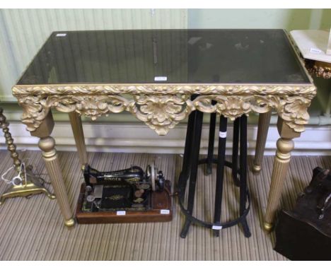 A MODERN SMOKED GLASS TOPPED CONSOLE TABLE on fancy gilded four legged base 