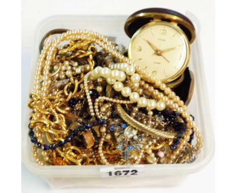 A tub containing a quantity of assorted costume jewelley necklaces and other items, also a vintage Stirling travelling alarm 