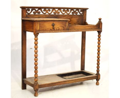 Early 20th Century oak stickstand with scroll pierced back over two divisions and drip tray beside a single drawer on bobbin 