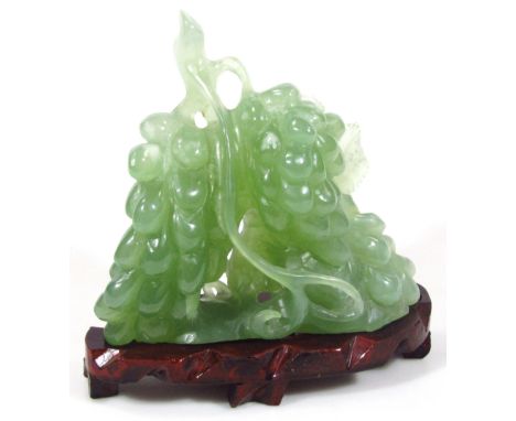 A modern green jade carving of bunches of grapes, on a carved wooden stand, 16cm high.
