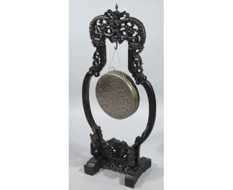 A Chinese dinner gong, heavily carved with inverted top, scroll and pineapple finial and shaped scroll feet, possibly hongmu 