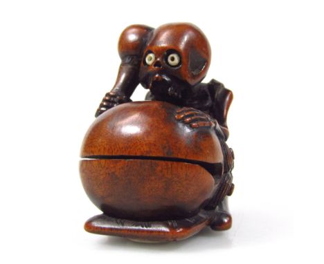 A Meiji period Japanese carved hardwood netsuke, in the form of a seated skeletal figure banging a drum, signed to the base, 