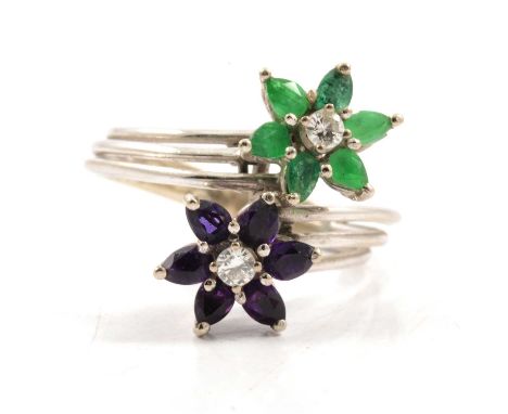 An emerald and amethyst dress ring, two floral heads set in a white metal crossover mount marked 14K and claw set with six ma