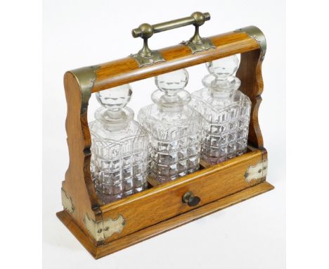 An Edwardian oak framed tantalus, with plated mounts, three moulded and cut finish glass decanters having facet cut stoppers,