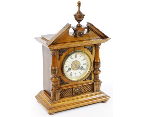 An Edwardian oak cased mantel clock, in an architectural case with broken pediment, surmounted by an urn finial, raised above