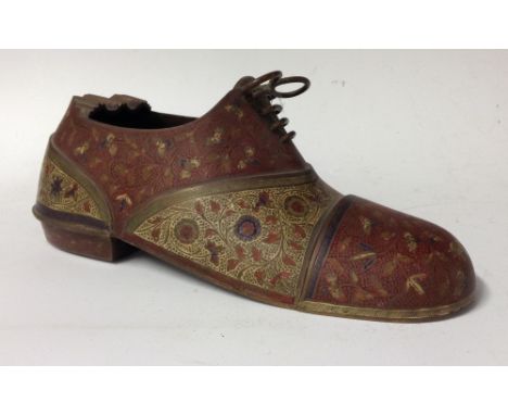 A Persian brass and enamel novelty cigar holder/ash tray, as a tied shoe, enamelled with alternating reserves of claret red a