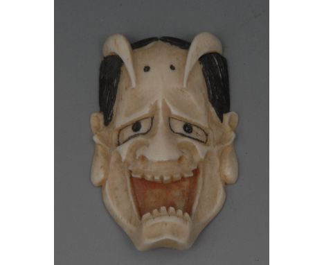 A Japanese ivory netsuke, carved as a grotesque noh mask, painted features, 4.5cm long, signed, Meiji period