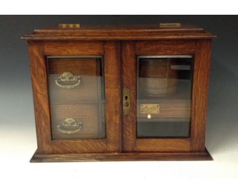 A Victorian oak smoker's compendium, a pair of bevelled glazed doors open to reveal two drawers flanked by a shelf with tobac