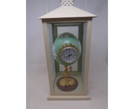 A hand painted ostrich egg clock with quartz movement on a figural base inside a hurricane lamp 