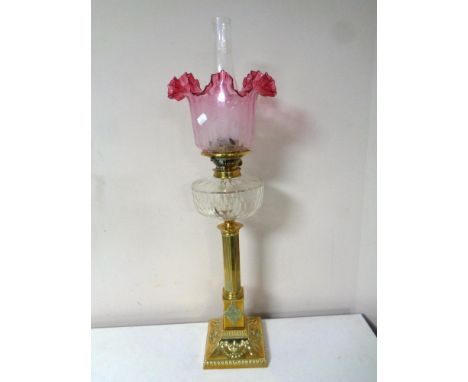 A brass Corinthian column oil lamp with etched cranberry glass shade, clear glass reservoir and chimney, height 79cm